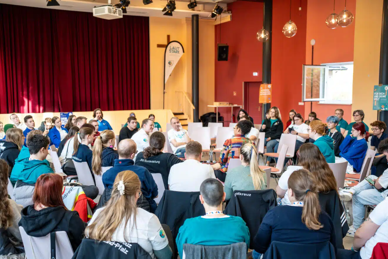 Etwa 100 junge Menschen sitzen in Form eines Atriums in einem Veranstaltungsraum und folgen einer Diskussion der Personen ganz innen.