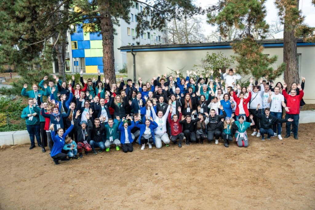 Etwa hundert Personen haben sich zu einem Gruppenbild aufgestellt, für das alle die Hände jubelnd hochheben.